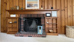 A fireplace with a brick surround, a framed picture above it, and a small lantern on the mantel. - Falmouth - walk to beach, walking path, close to downtown, private yard (Falmouth)