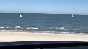 A beach with two sailboats in the distance and a clear sky.