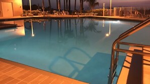 A swimming pool with lounge chairs and palm trees at dusk.