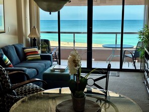 A living room with a sofa, a table with a vase, and a view of the beach and ocean through large windows. - A Touch Of Paradise On Earth (Clearwater)