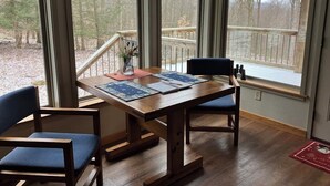 A dining area with a wooden table and chairs, large windows with a view of trees and a deck. - Private & unplugged.  Near Fallingwater, GAP and Ohiopyle. 5-star reviews (Fort Hill)
