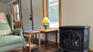 A cozy living room with a green patterned sofa, a small wooden table with a lamp, and a black wood-burning stove. - Private & unplugged.  Near Fallingwater, GAP and Ohiopyle. 5-star reviews (Fort Hill)