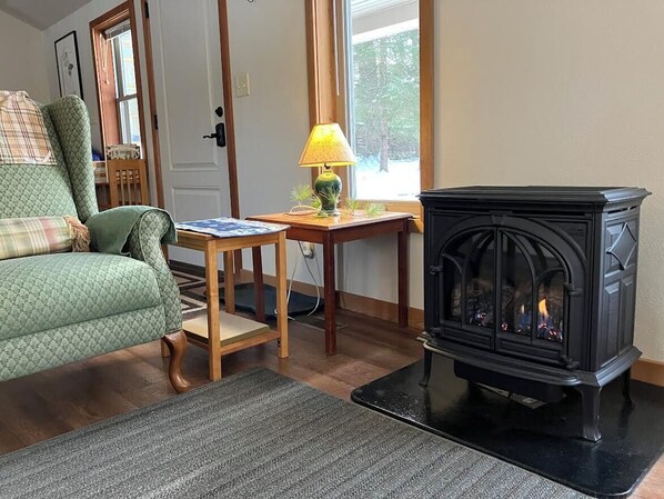A cozy living room with a green patterned sofa, a small wooden table with a lamp, and a black wood-burning stove. - Private & unplugged. Near Fallingwater, GAP and Ohiopyle. 5-star reviews (Fort Hill)