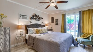 Ein Schlafzimmer mit einem Bett, einem Deckenventilator, einem Nachttisch mit Lampe, Wanddekoration und einem Fenster mit Vorhängen.