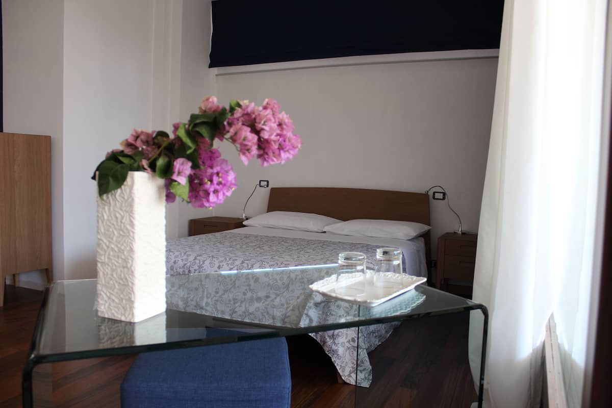 Een hotelkamer met een bed, nachtkastje en een glazen tafel met een bloemenvaas.