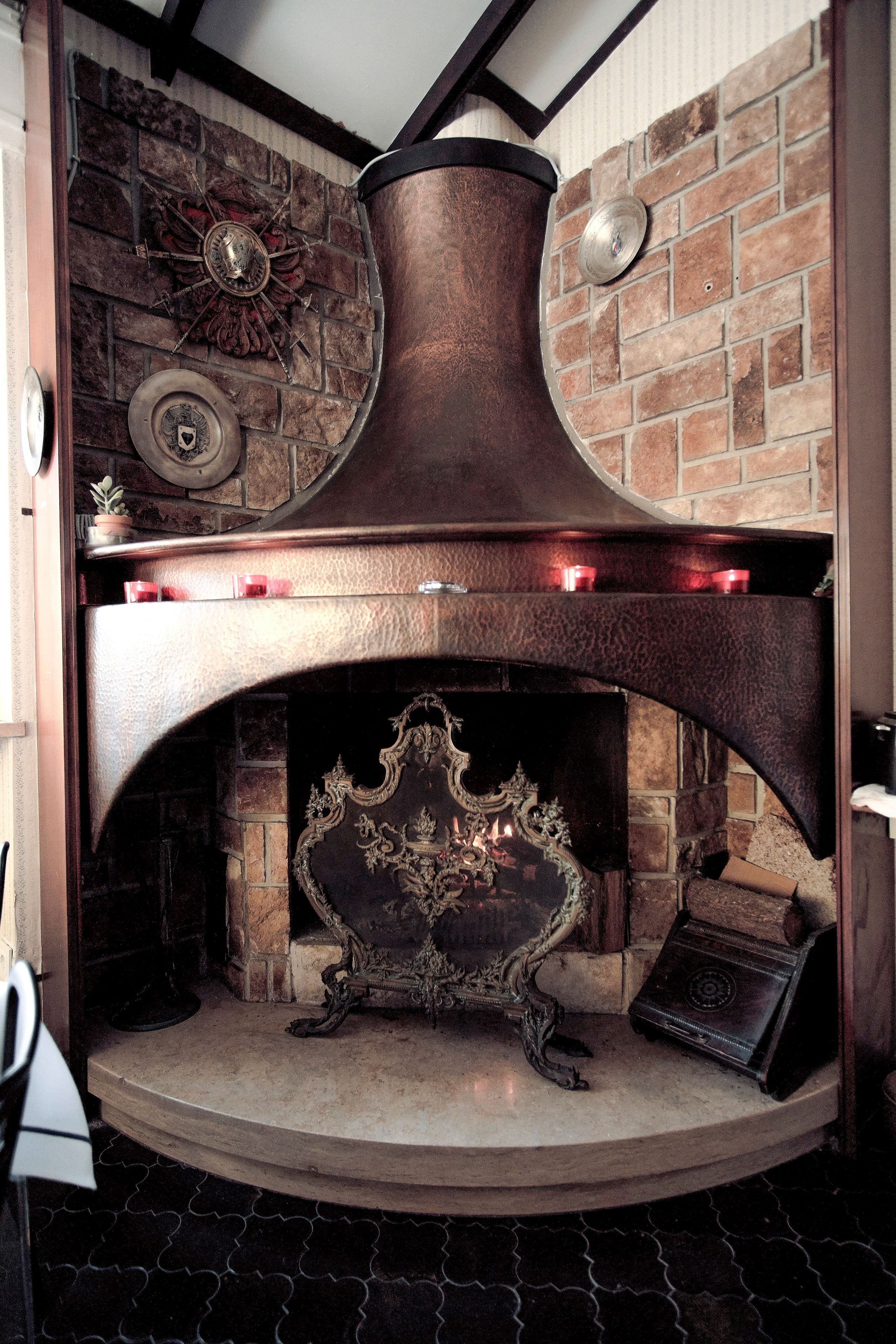 A fireplace with a stone mantle, a decorative clock, and a metal vent above it.