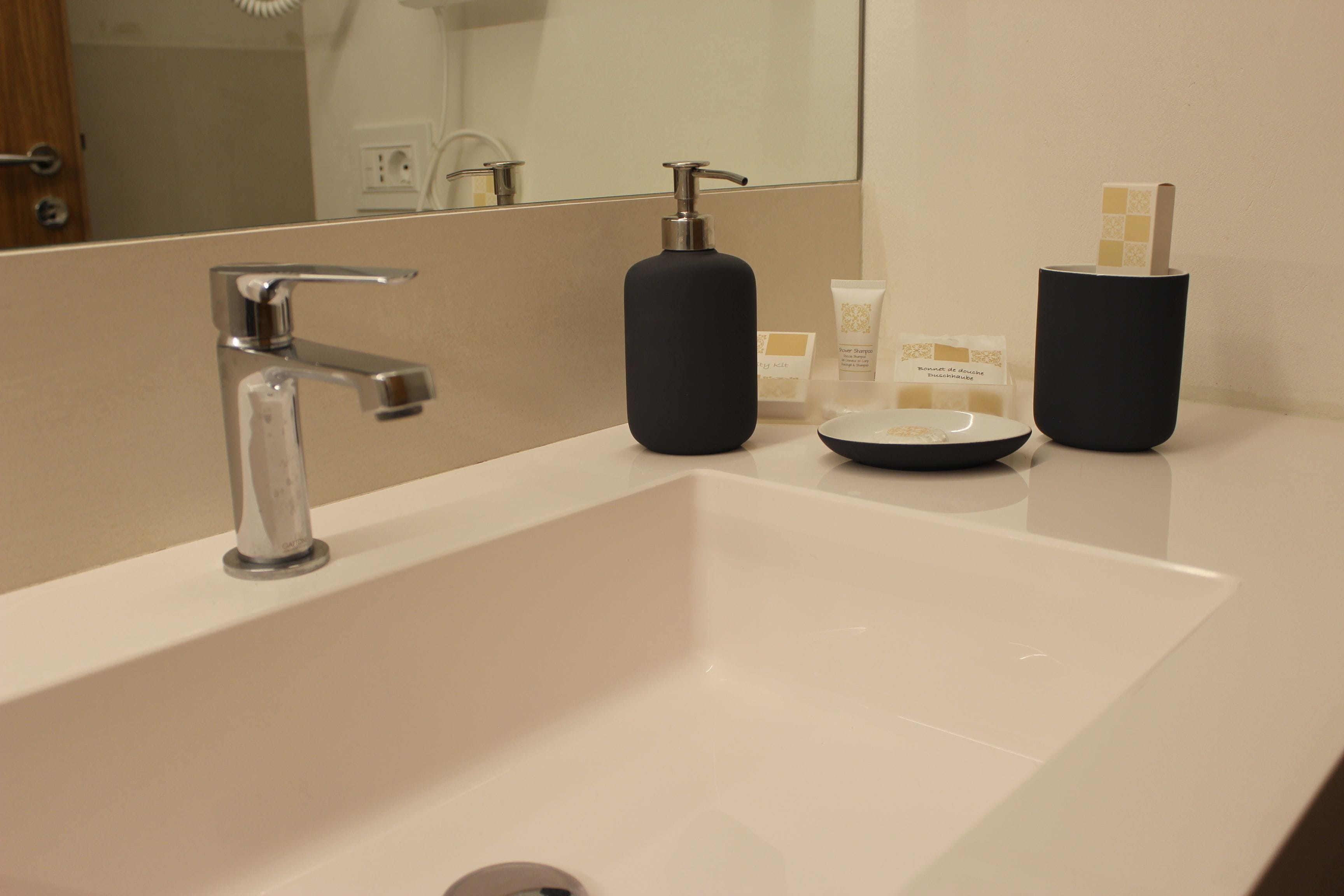 A modern bathroom with a white sink, a chrome faucet, and two black soap dispensers.