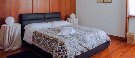 A bedroom with a wooden headboard, a bed with a patterned bedspread, a bedside table with a lamp, and a small side table with a decorative item.