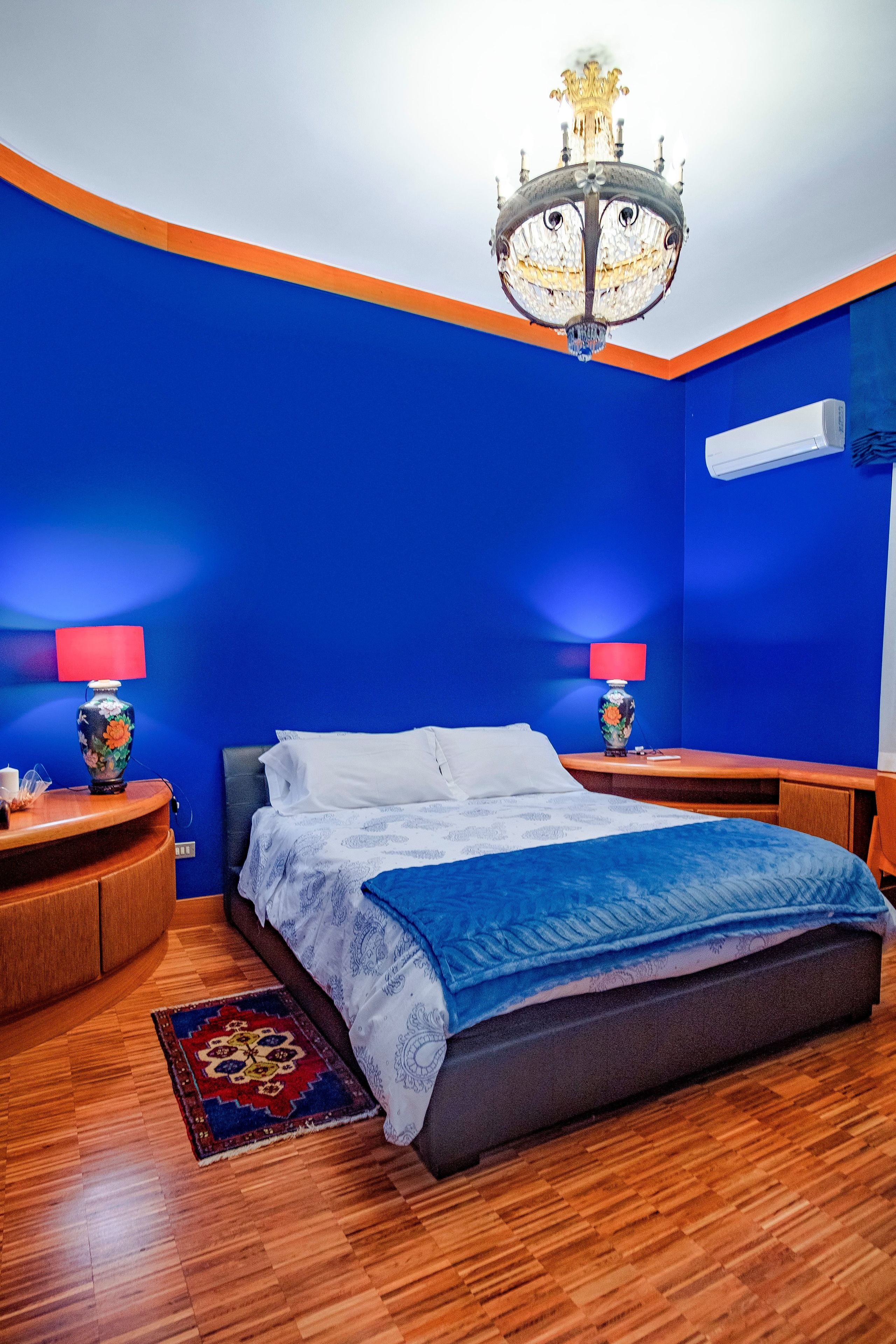 Un dormitorio con cama, dos mesitas de noche con lámparas, una araña y una pared azul.