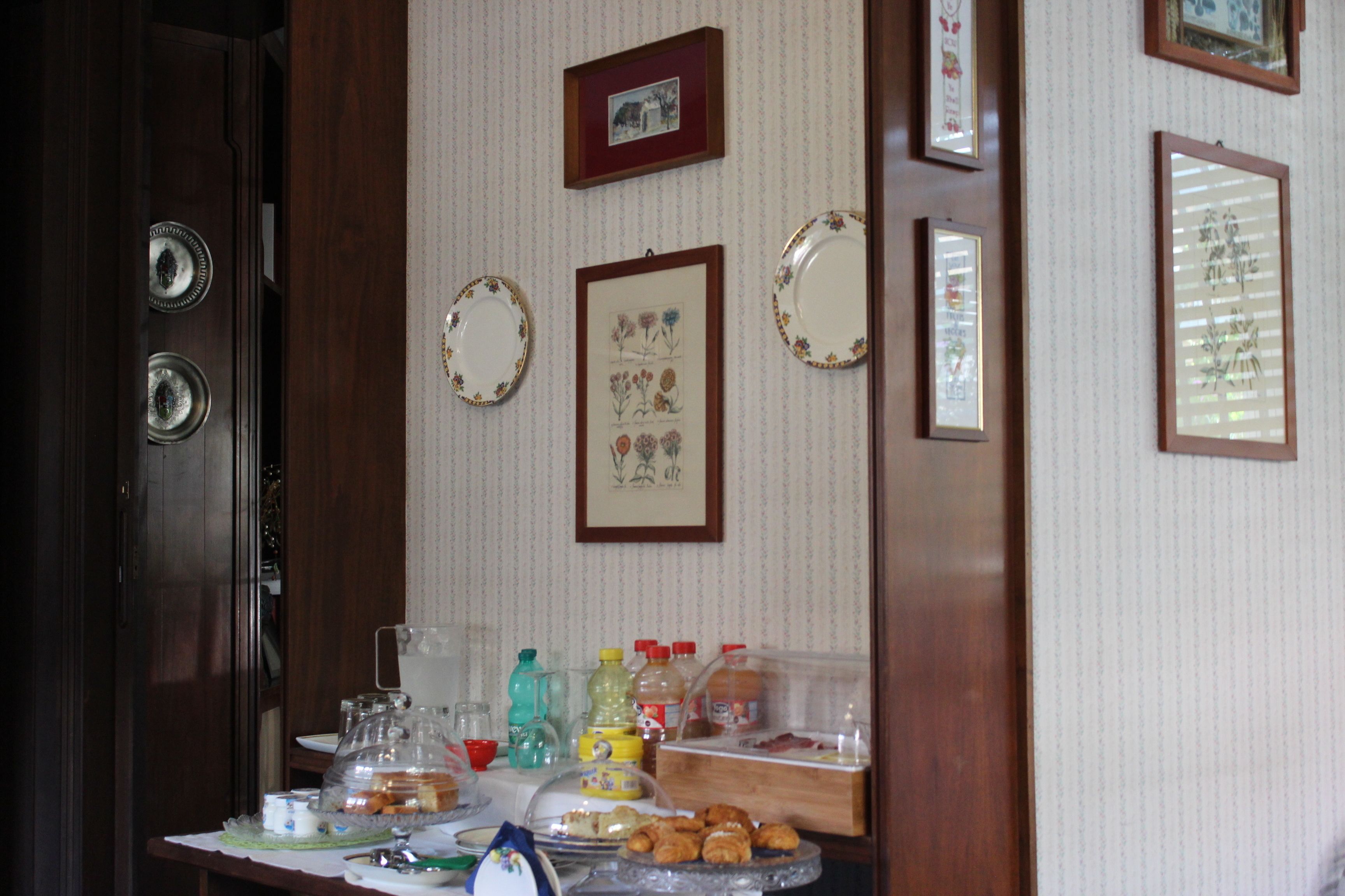 Una tavola imbandita per la colazione, con diversi cibi e condimenti, stampe floreali alle pareti e una porta in legno.