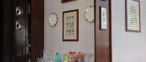 A breakfast table with various food items and condiments, framed botanical prints on the wall, and a wooden door.