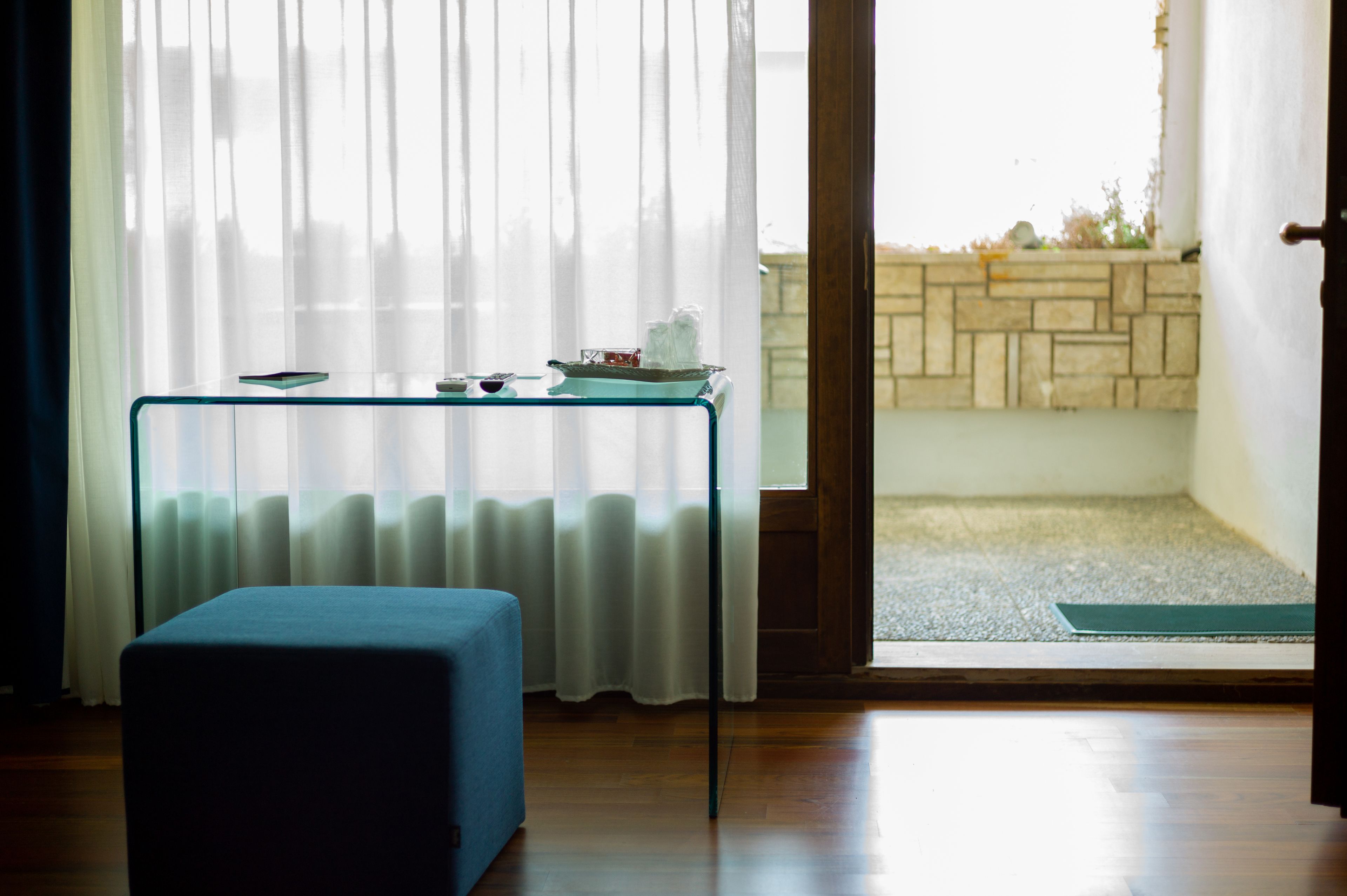 A room with a glass table, a blue bench, a view through a door to a balcony with a stone wall.