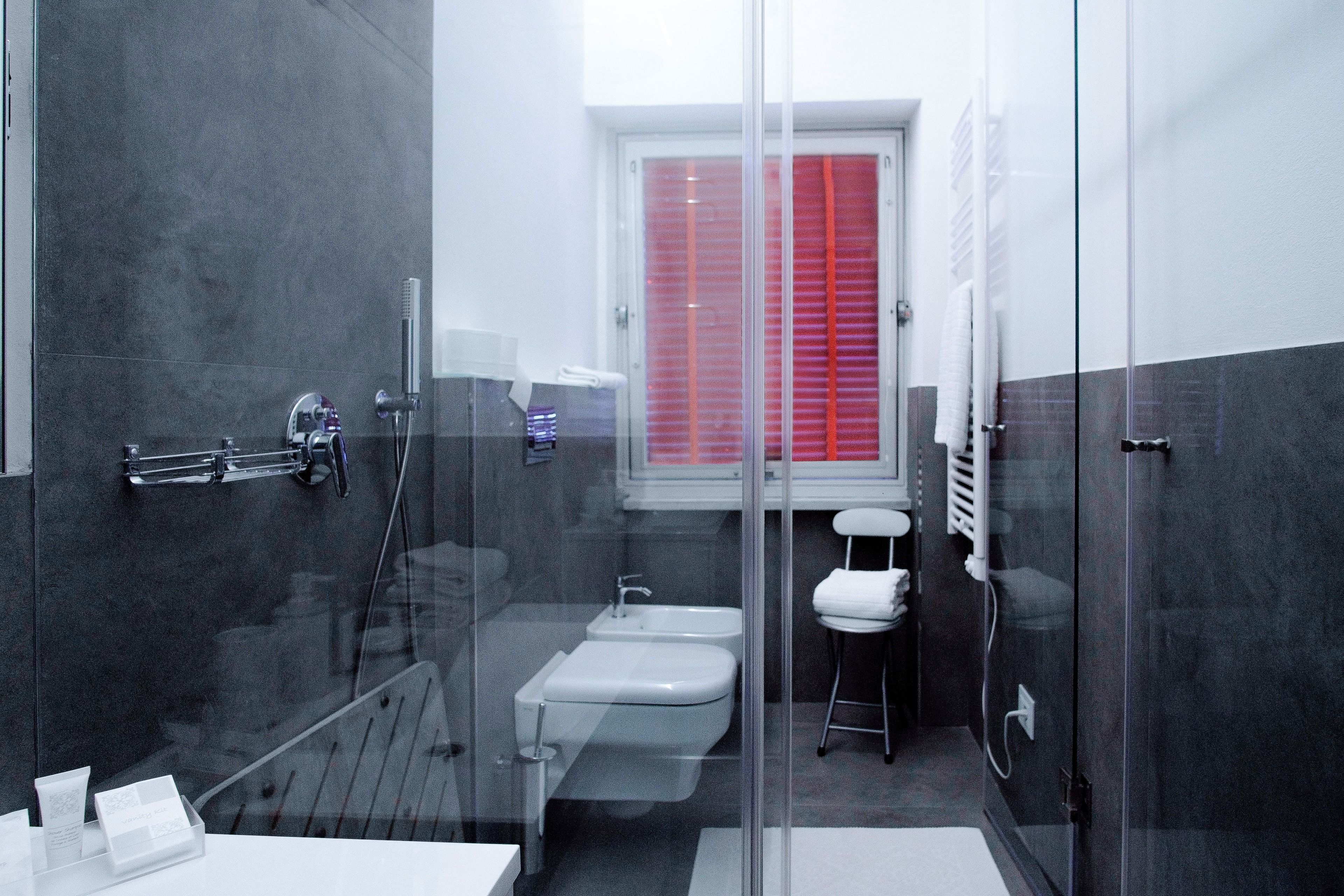 Ein modernes Badezimmer mit Duschkabine aus Glas, einem weißen Waschbecken und einem Fenster mit rotem Rahmen.
