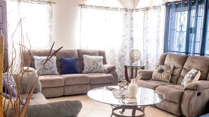 A living room with a beige sofa, a glass coffee table, and a blue curtain.