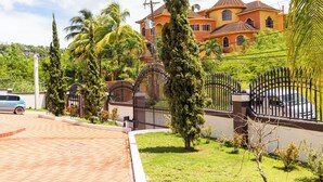 A large house with a gated driveway, surrounded by palm trees and a well-maintained lawn.