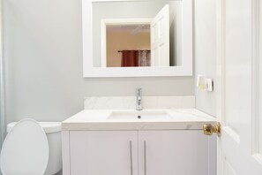 Un baño con lavamanos blanco, espejo, inodoro y puerta con manija de latón.