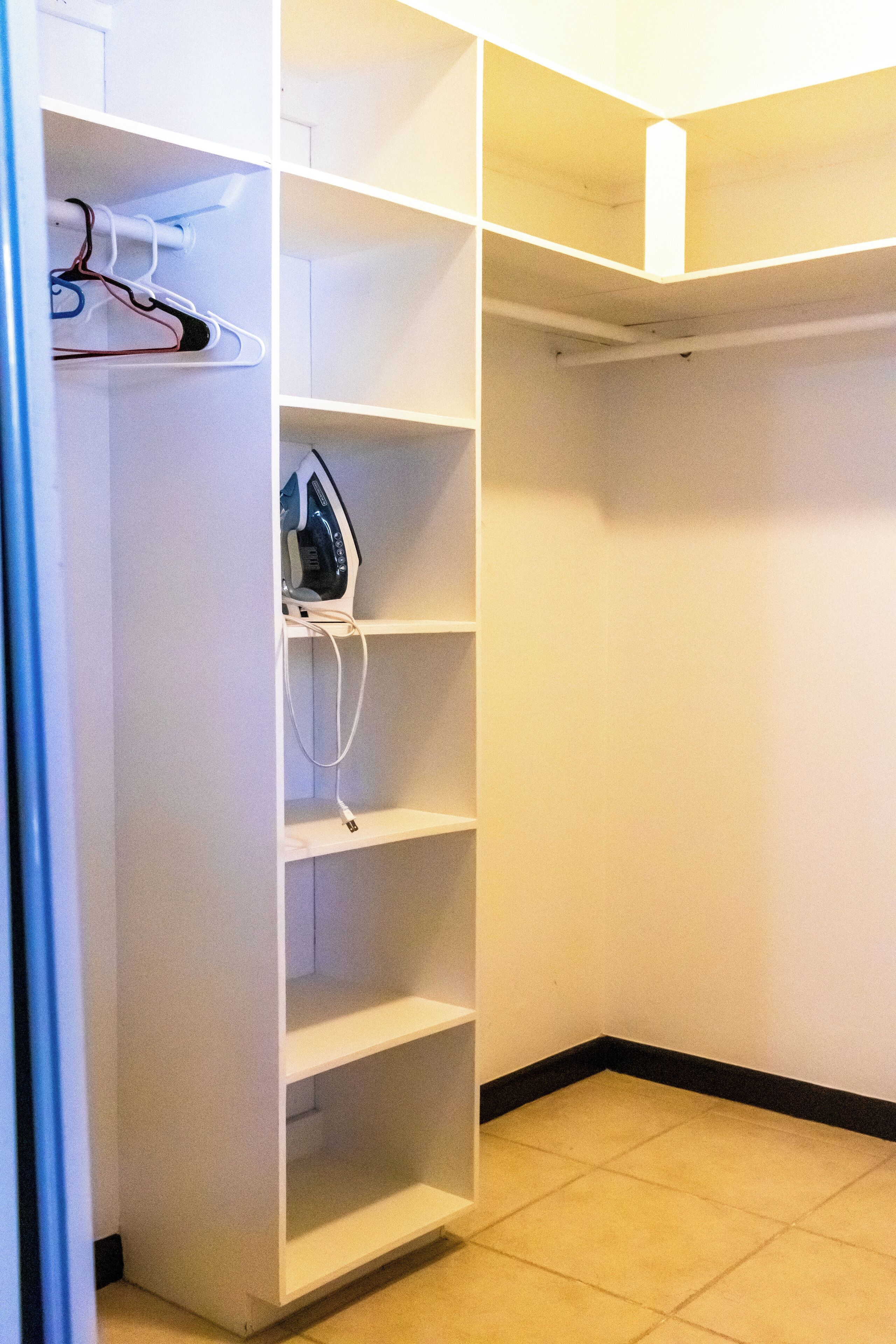 Un dressing avec de nombreuses étagères et un espace pour suspendre les vêtements, comprenant un fer à repasser blanc et une multiprise.