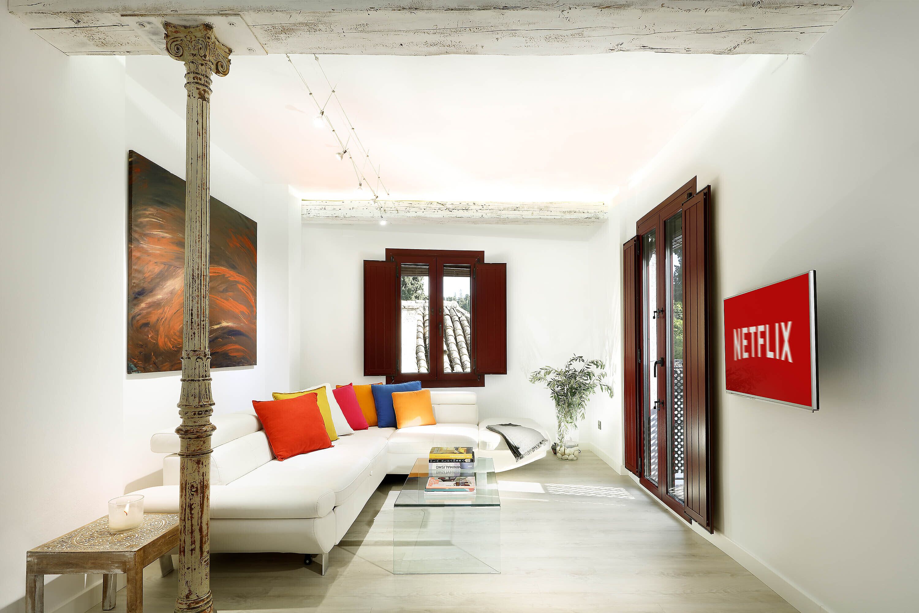 A modern living room with a white sofa, colorful cushions, a glass coffee table, and a large painting.