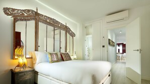 Een slaapkamer met een groot bed, een versierd hoofdeinde, een bedlampje en zicht op een andere kamer.