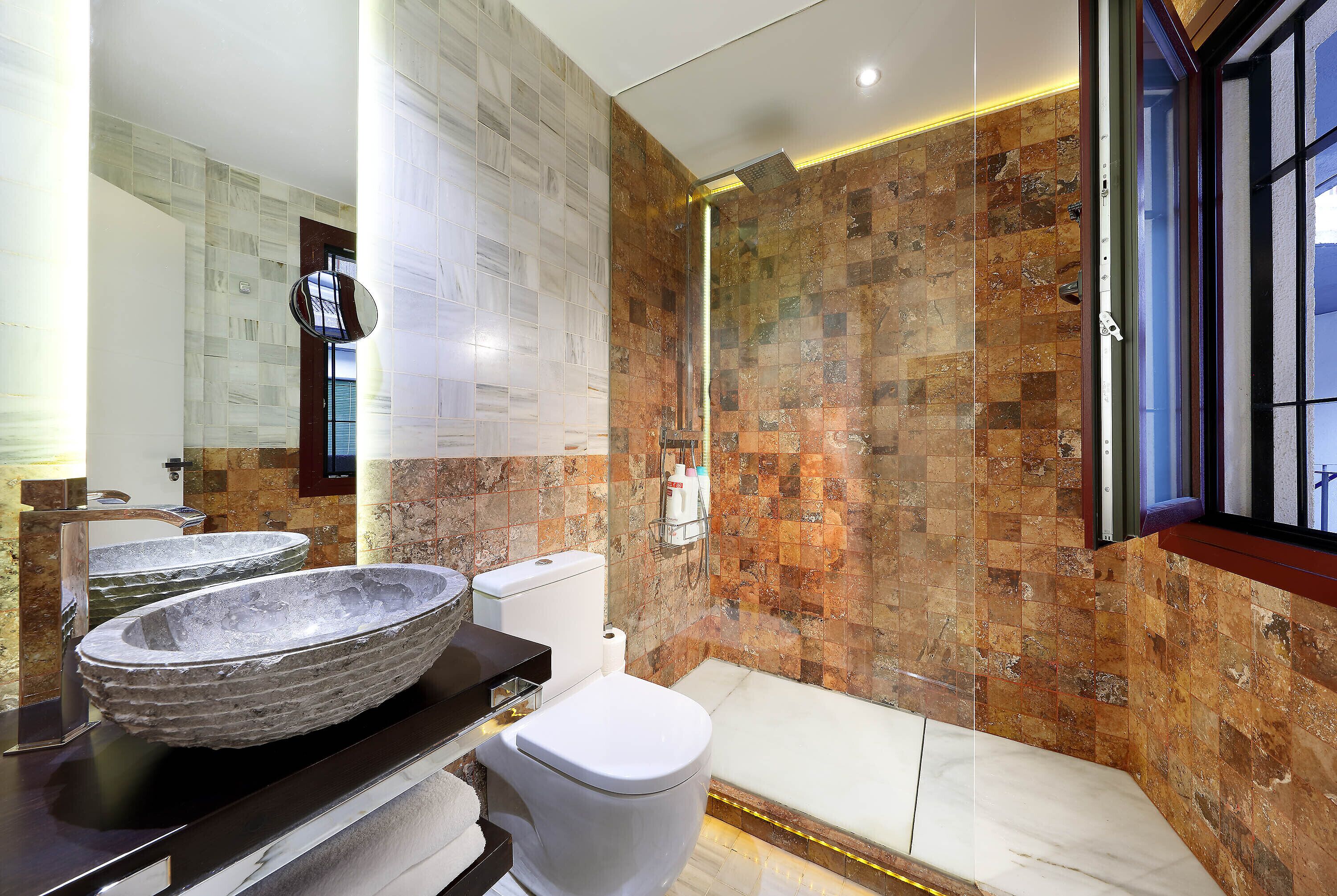A modern bathroom with two stone sinks, a toilet, and a shower.