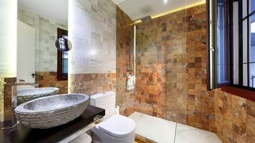 A modern bathroom with two stone sinks, a toilet, and a shower.