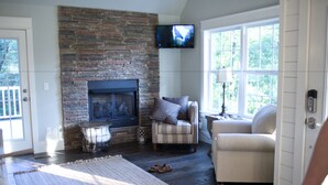 A living room with a stone fireplace, a television mounted above it, and two armchairs. - Stonehill Cottages (Mena)