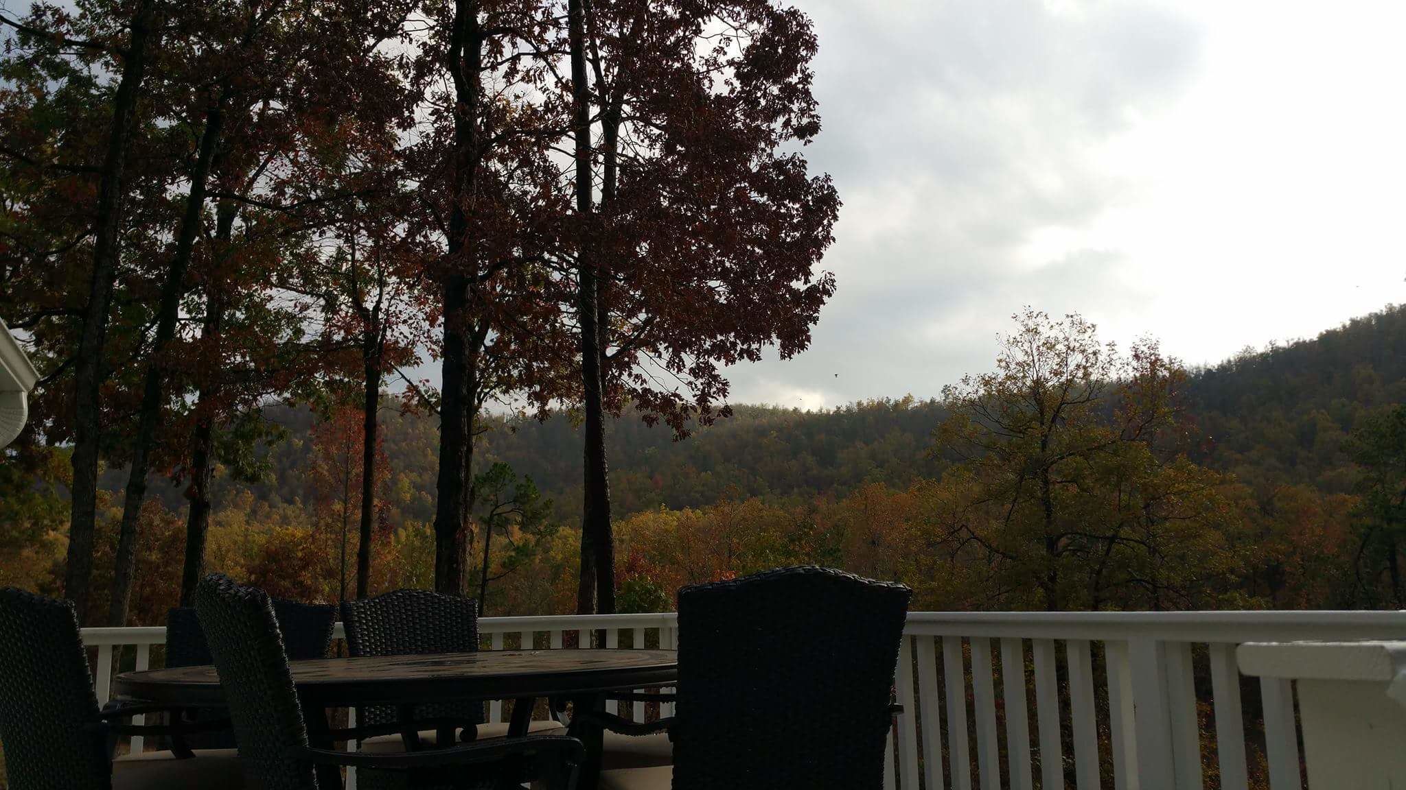 A deck with outdoor seating and a view of a forested hillside.