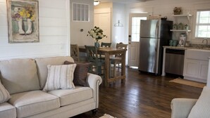 A living room with a sofa, chairs, a dining table, and a kitchen area with a refrigerator and cabinets. - Stonehill Cottages (Mena)