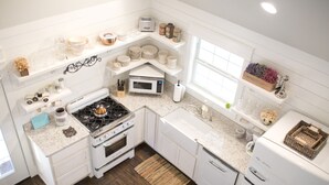 A modern kitchen with white cabinetry, a gas stove, a microwave, and a refrigerator. - Stonehill Cottages (Mena)