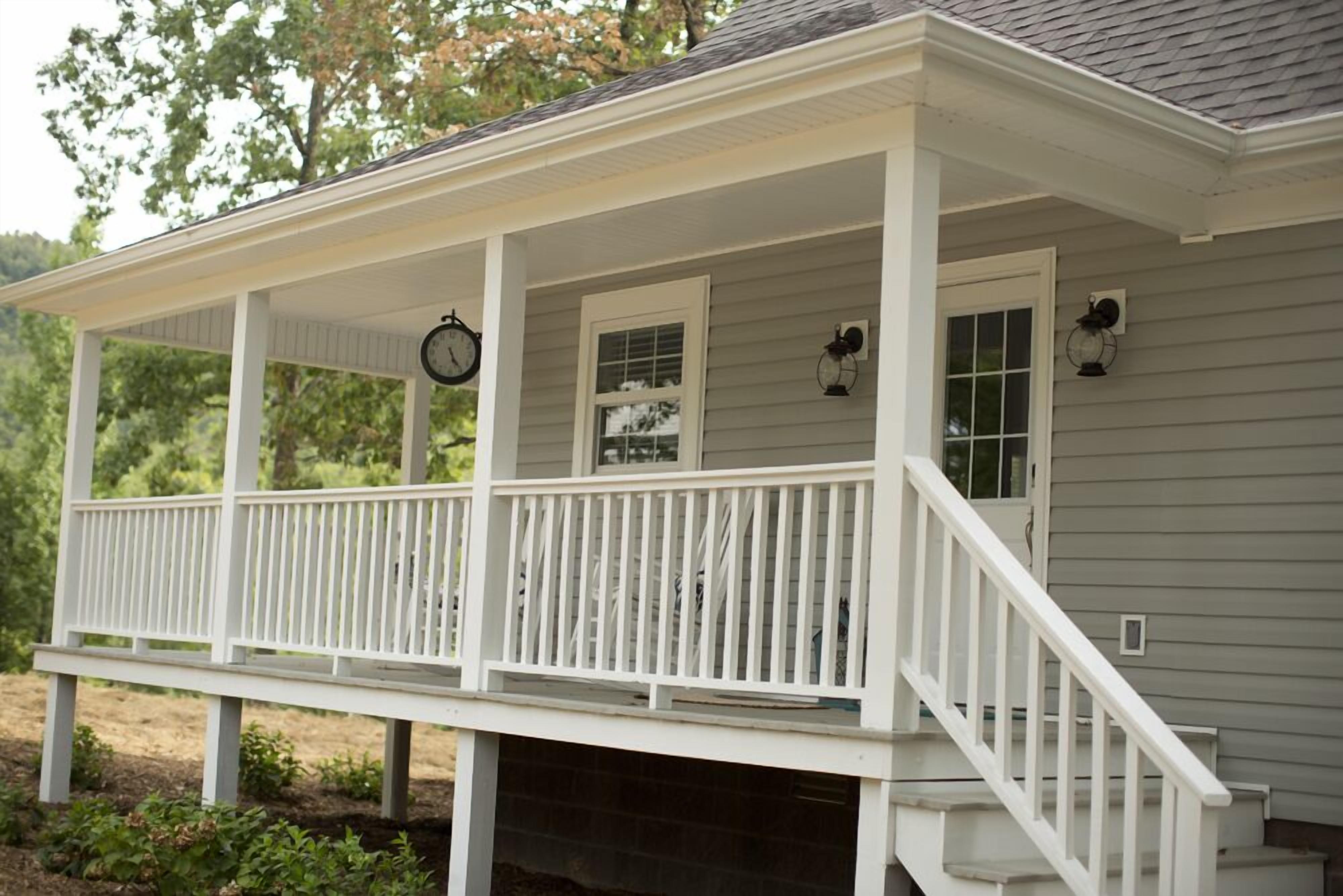 A white porch with a railing, a clock, and two wall-mounted lanterns.