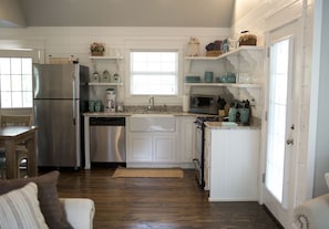 A modern kitchen with white cabinetry, stainless steel appliances, and a window providing natural light. - Stonehill Cottages (Mena)