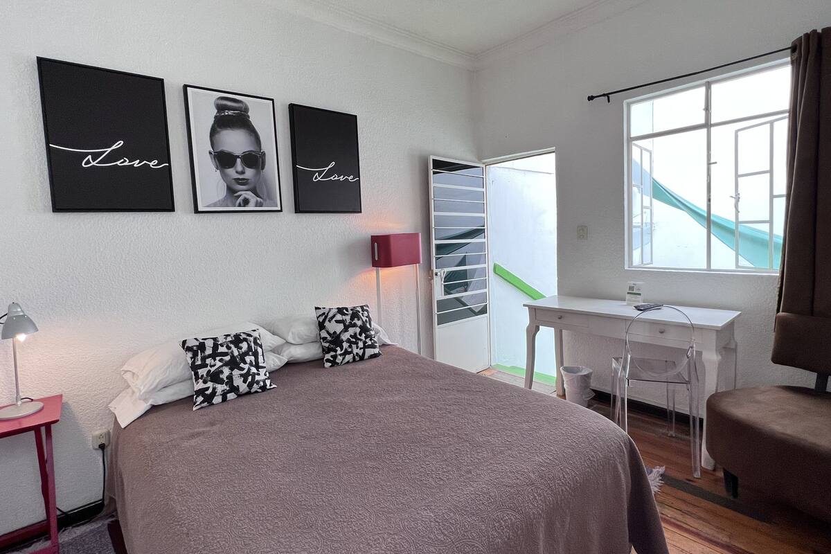 A bedroom with a bed, a desk, and a window.
