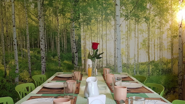 Une table à manger dressée avec des assiettes, des verres et un vase contenant une rose, le tout sur fond d’un décor inspiré de la forêt.