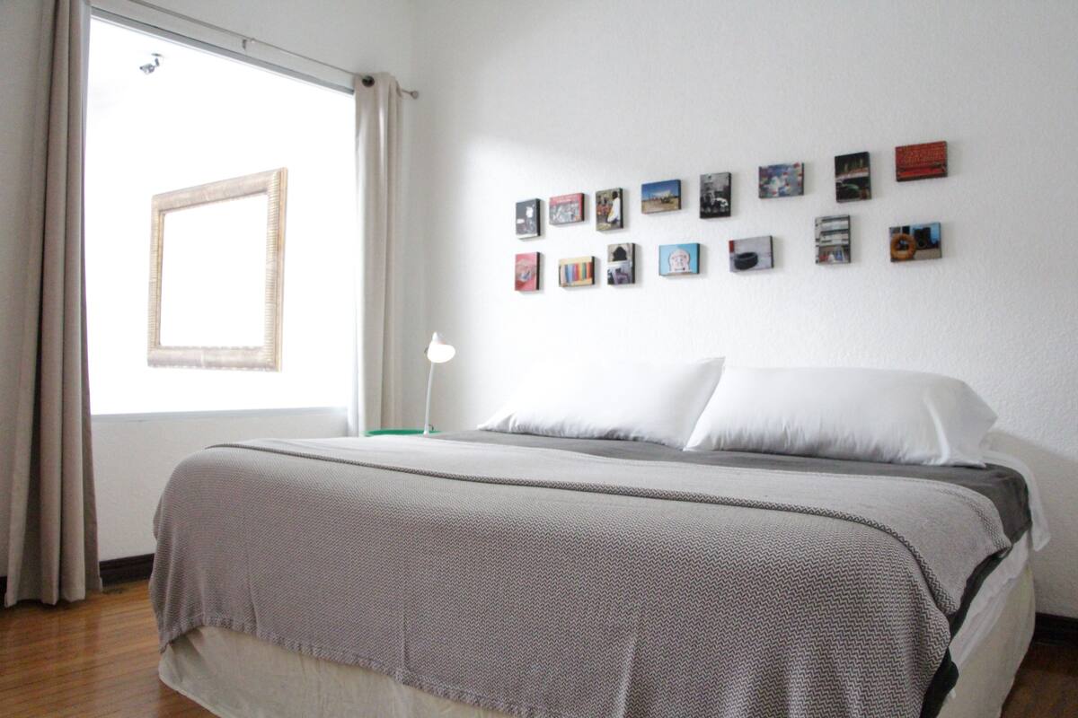 A neatly made bed with a grey and white patterned bedspread, a white pillow, and a bedside table with a lamp.