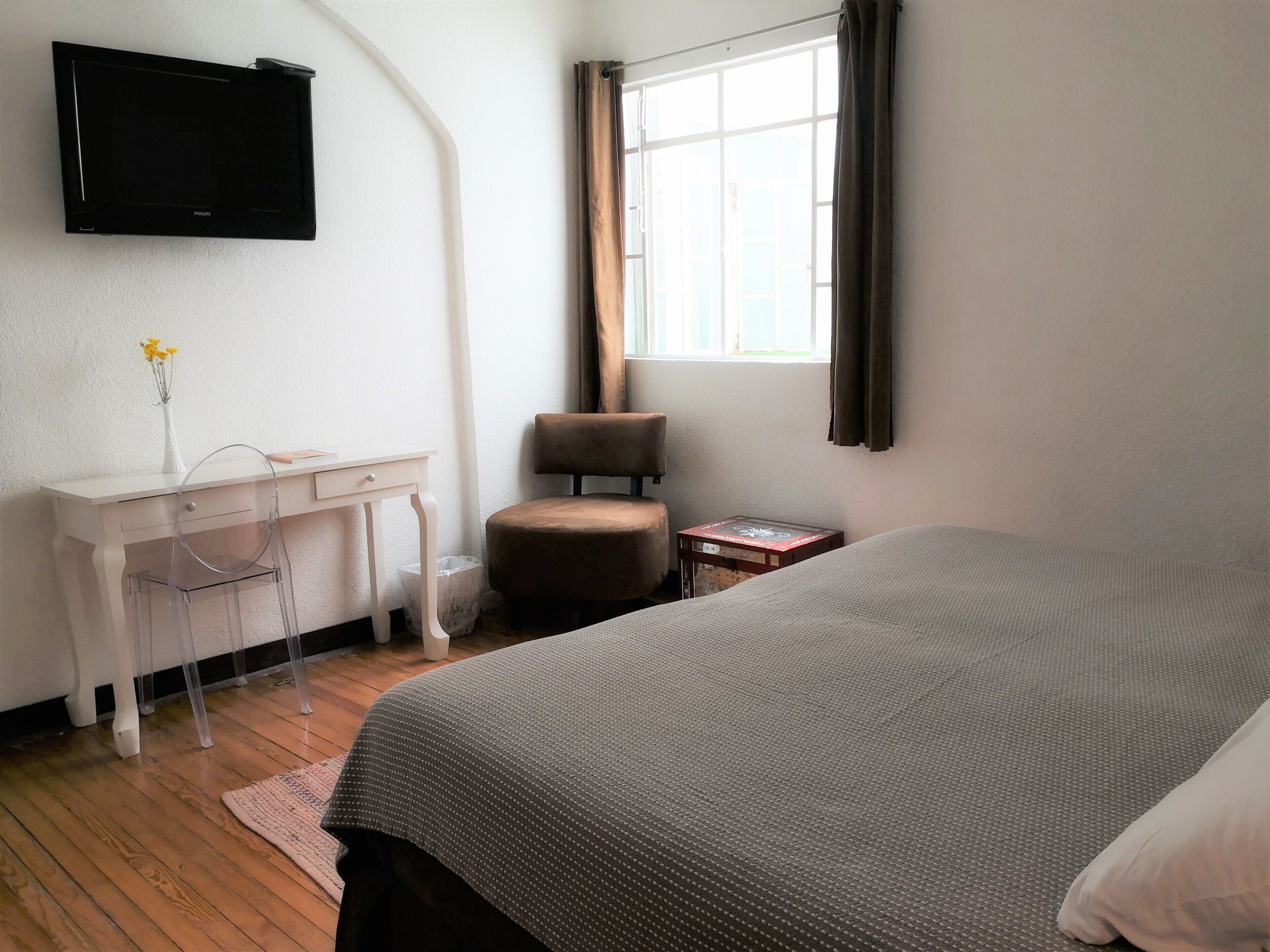 Een hotelkamer met een bed, een bureau met stoel, een aan de muur bevestigde televisie en een raam met gordijnen.