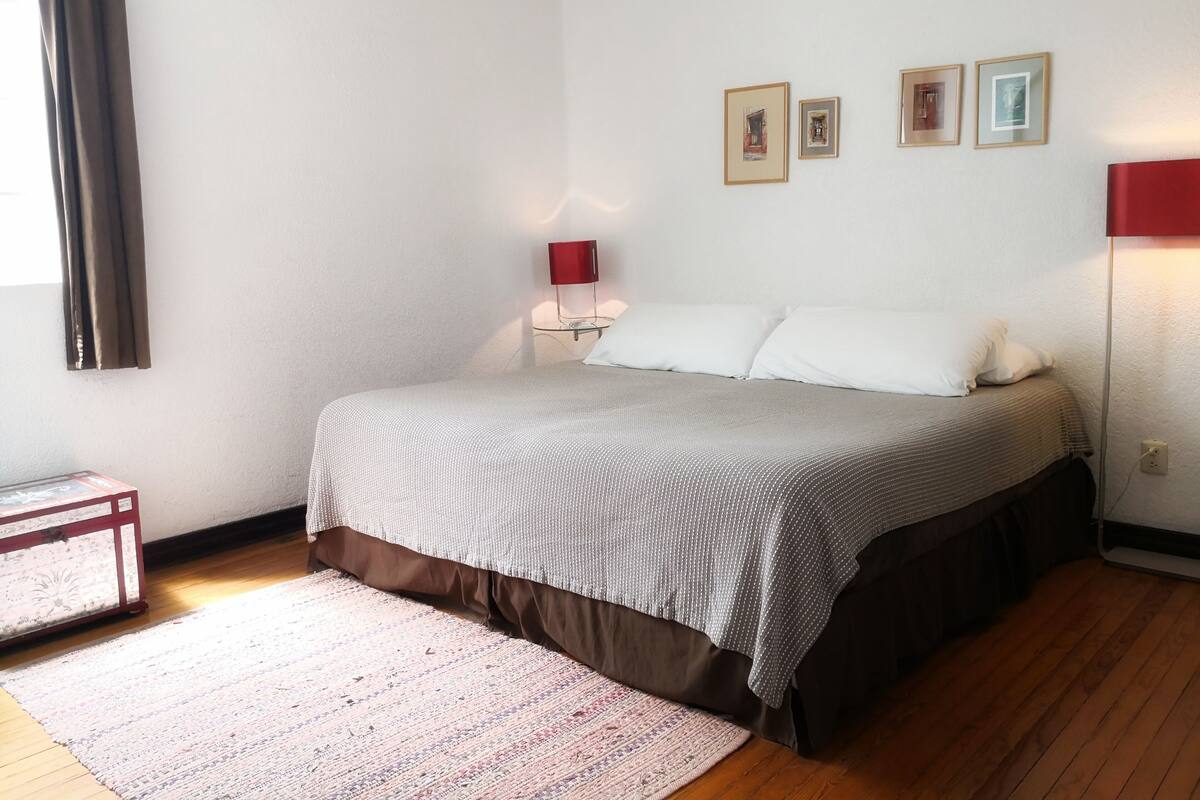 A neatly arranged bedroom with a bed, bedside tables, a lamp, and framed pictures on the wall.