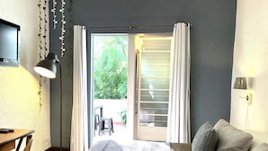 Une chambre à coucher comprenant un lit, un bureau, une chaise, un canapé et donnant sur l’extérieur grâce à une porte coulissante.