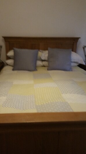 Una cama con cabecera de madera, dos almohadas y colcha.