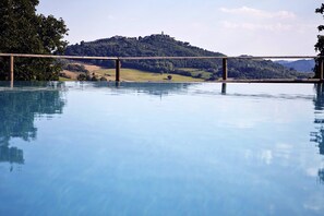 A clear view of a swimming pool with a wooden deck in the foreground and a hill with buildings in the background. - Authentic stone farmhouse, pool, view, bbq, wifi, bedrooms with bathroom and a/c (Resina I)