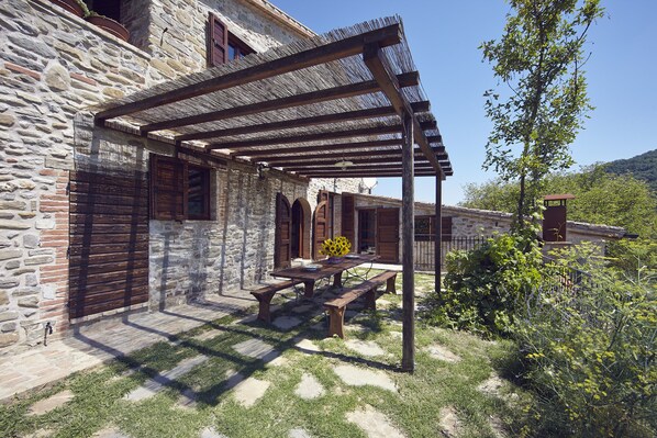 A stone building with a wooden pergola, a picnic table, and benches.