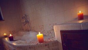 Et badeværelse med badekar, to tændte stearinlys og en bruser.