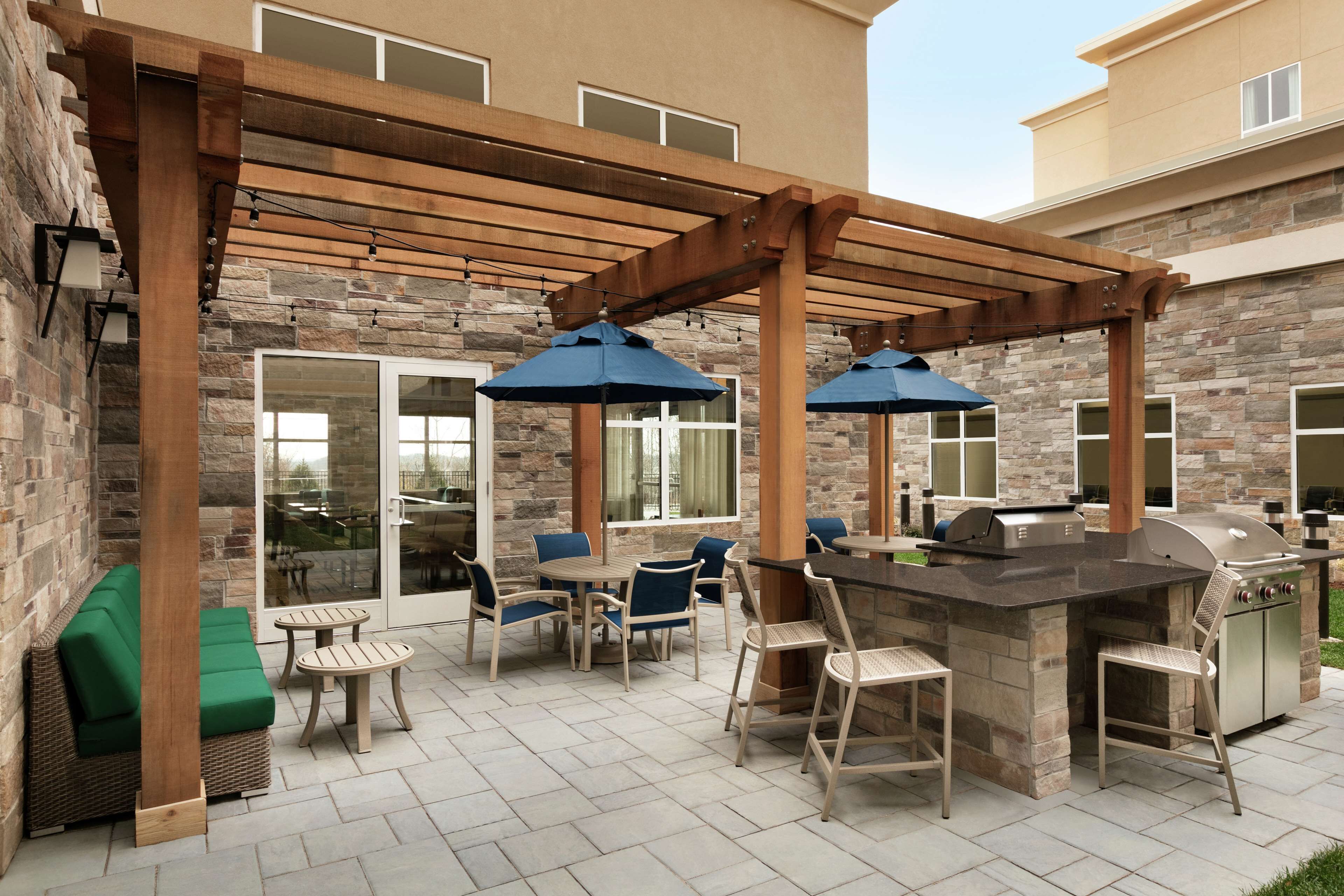 An outdoor patio with a stone wall, wooden pergola, and a barbecue area.