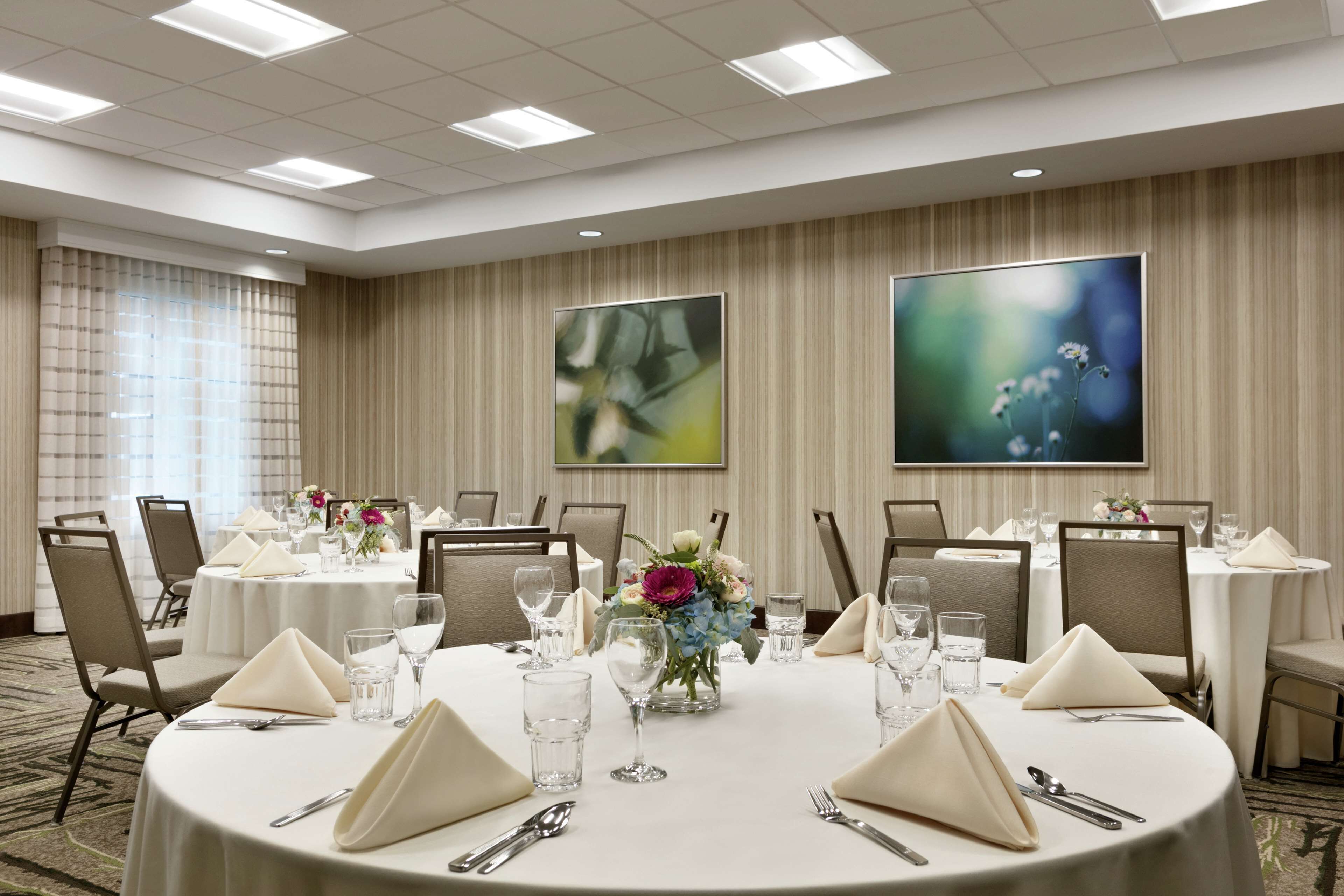 Un salón de conferencias con mesas redondas, sillas y centros de mesa con flores.