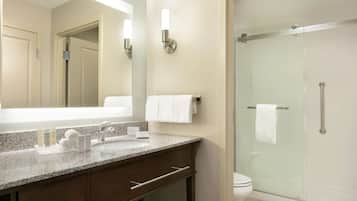 A modern bathroom with a granite countertop, a large mirror, a glass-enclosed shower, and a toilet.