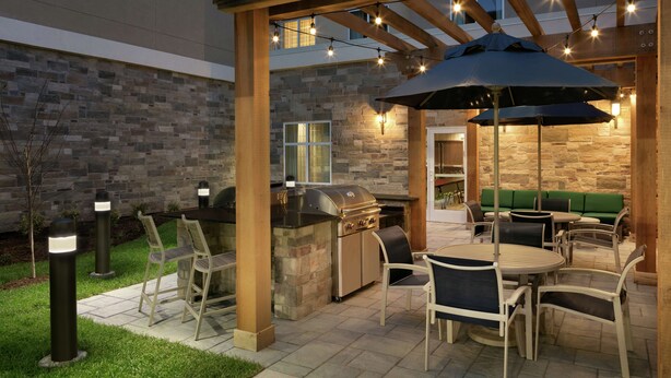 Een terras buiten met een stenen muur, een barbecue en tuinmeubilair.