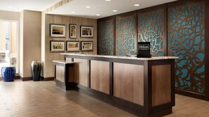 Een hotel receptie met een houten receptiebalie, ingelijste foto’s aan de muur en een ‘Hilton Honors’ bord.