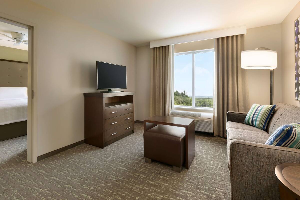 Een hotelkamer met een bed, een televisie op een dressoir, een bank met kussens, een bijzettafeltje en een raam met gordijnen.