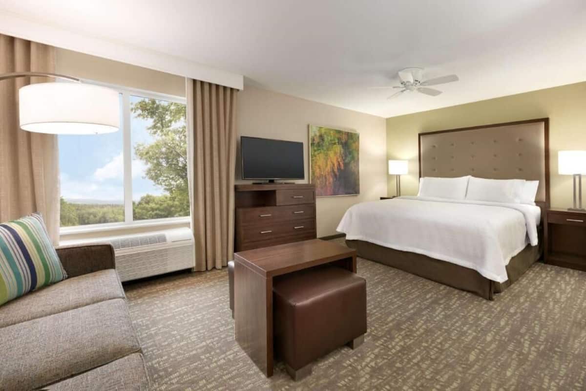 A hotel room with a bed, a TV, a desk, a chair, and a window with curtains.