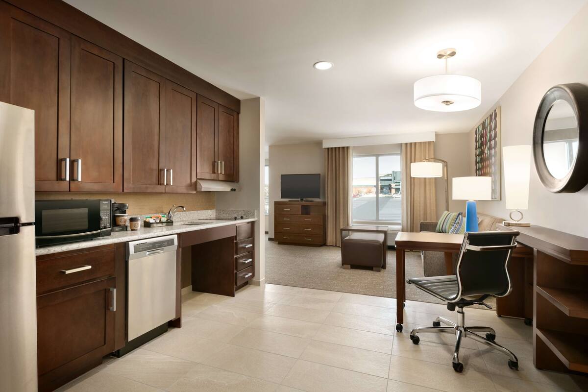 Een moderne hotelkamer met kitchenette, eethoek, grote spiegel en televisie.