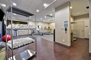 A hotel gym with exercise equipment, a towel rack, and a guest laundry sign.